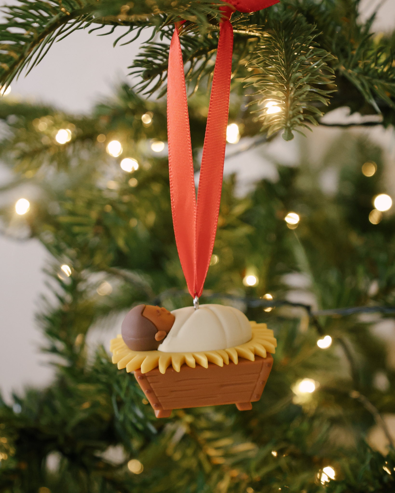 Baby Jesus Christmas ornament made of shatterproof resin with red ribbon, ideal holiday gift for children.