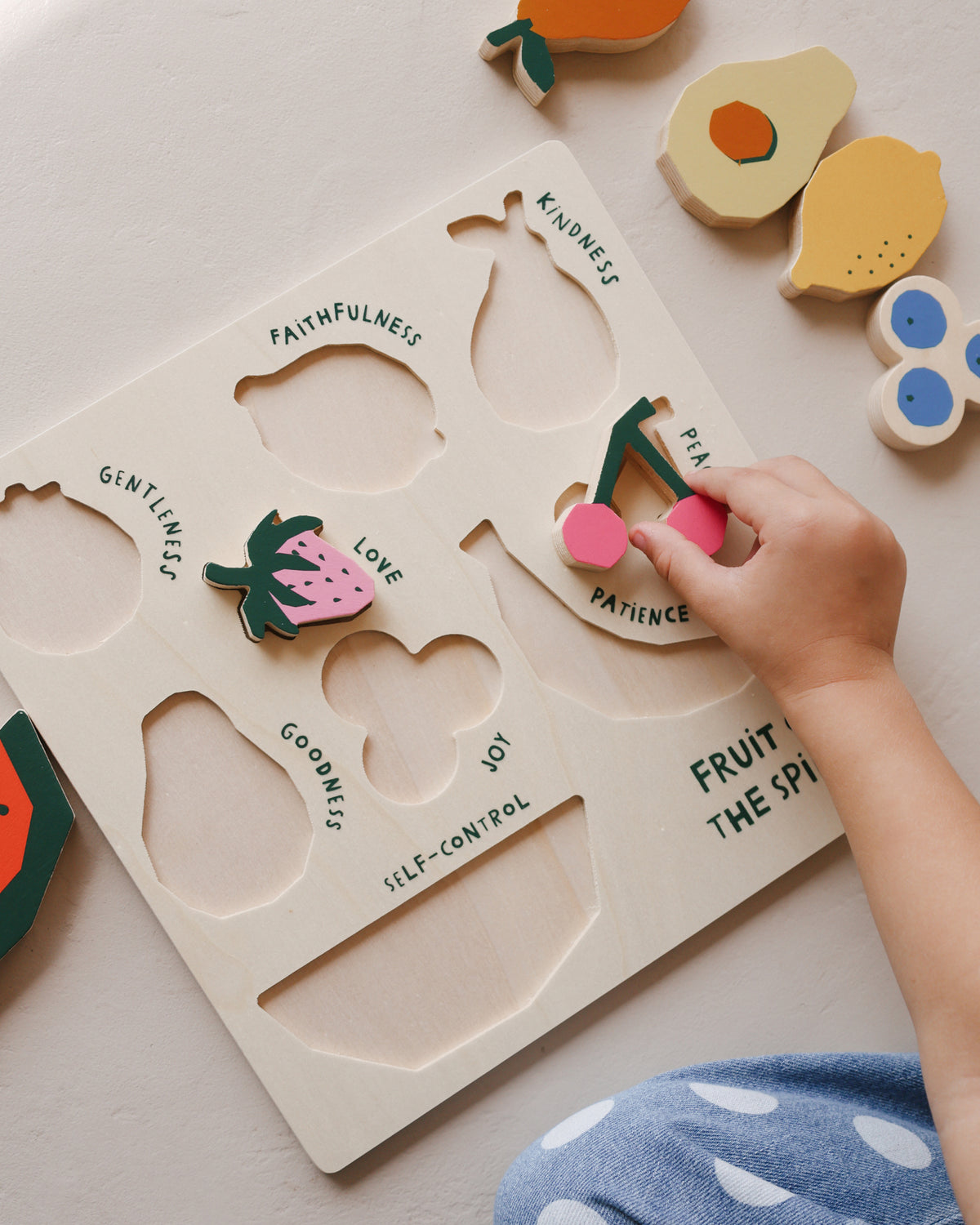 Child's hand fitting the strawberry into the Fruit of the Spirit wooden puzzle