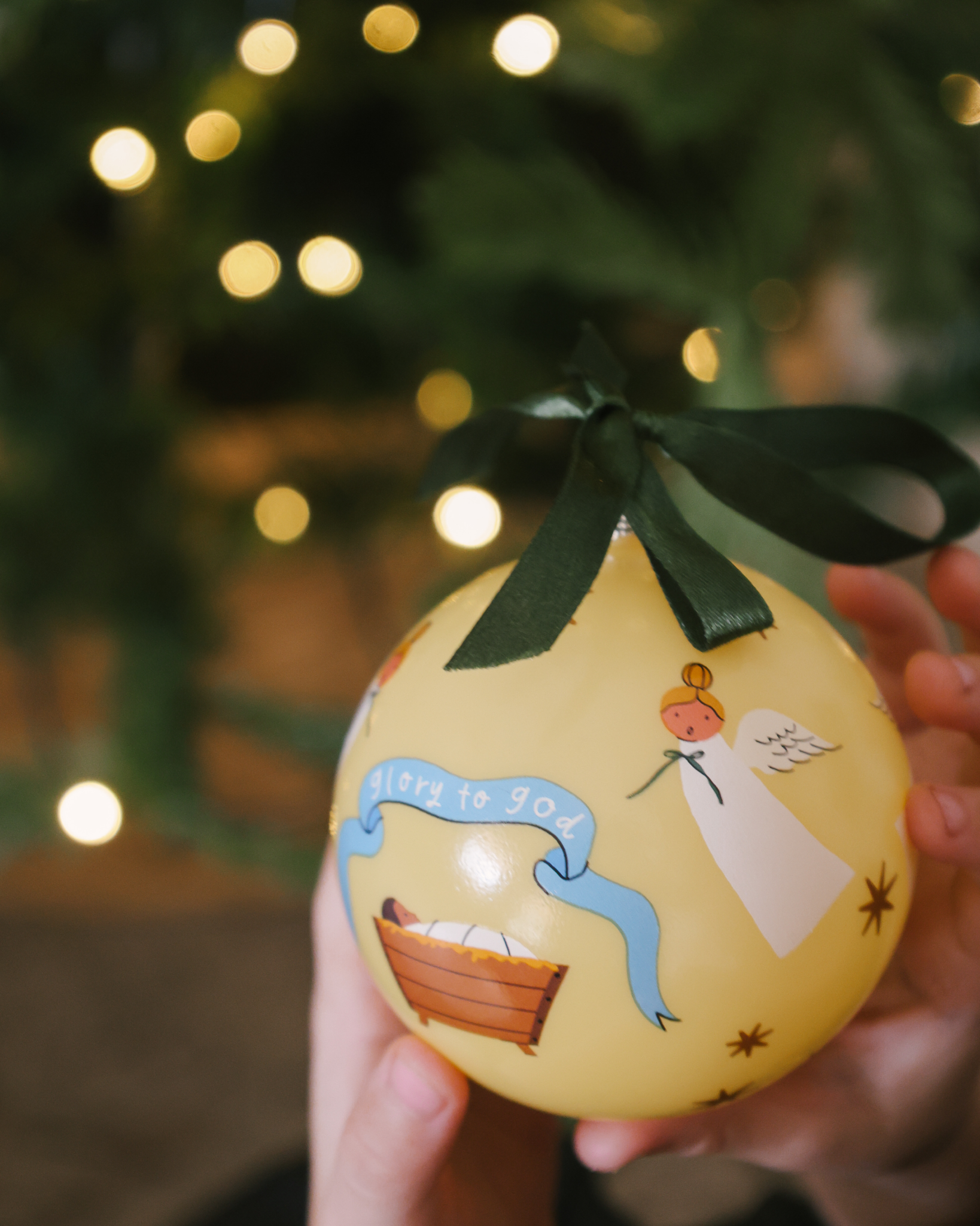 Glory to God Christmas ornament showing baby Jesus in the manger surrounded by angels, with satin ribbon hanger. Made of shatterproof plastic, ideal for families.