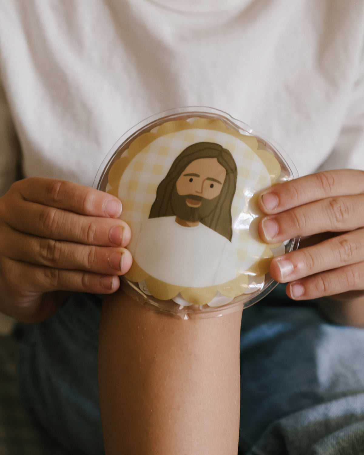 Child holding a yellow gingham Jesus Heals ice pack on his arm