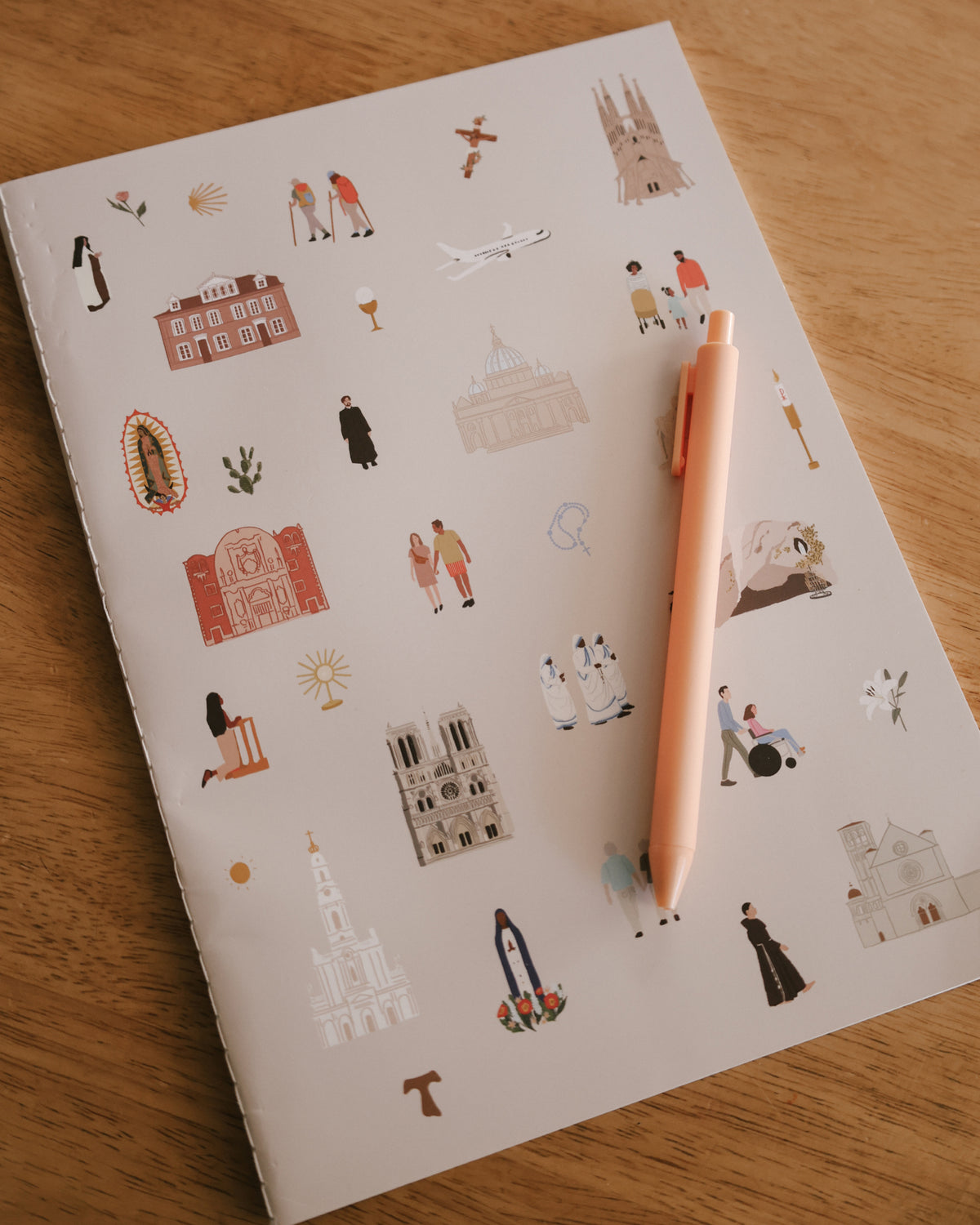 Catholic Pilgrimage Journal with a pen, cover pattern of pilgrimage sites and saints