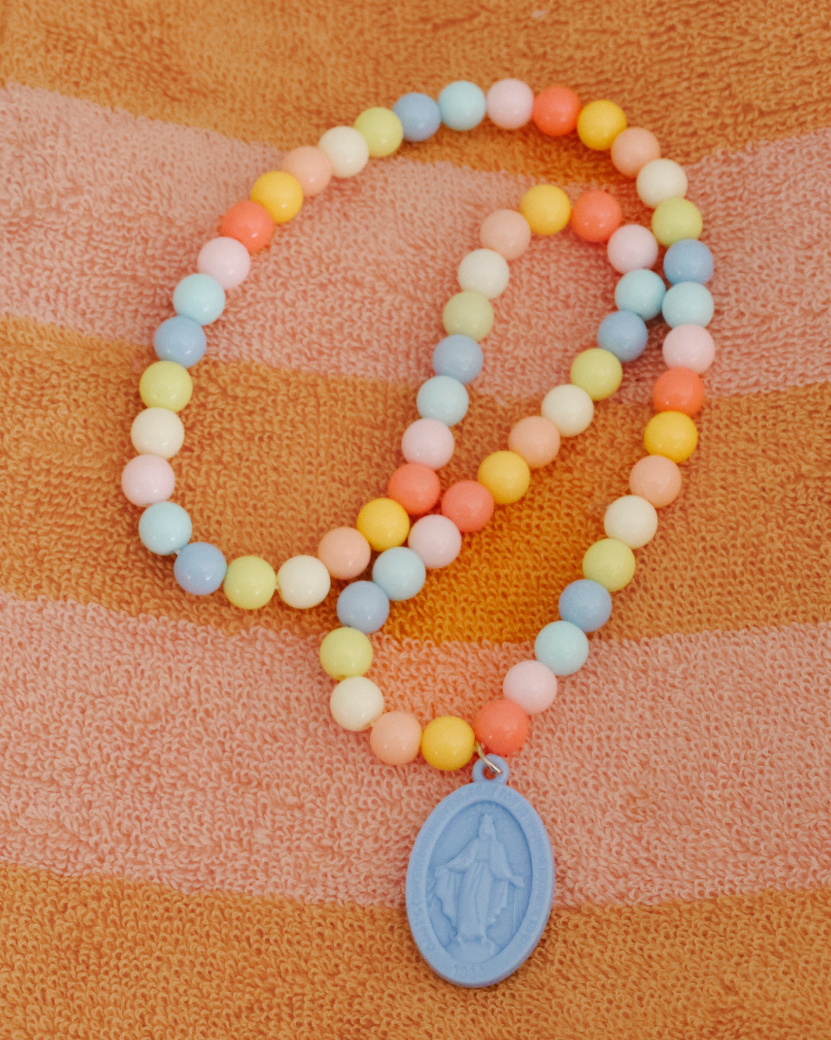Children’s Miraculous Medal necklace with soft blue medal and colorful plastic beads on elastic strand. Christian kids’ jewelry for Marian devotion, First Communion, or faith-based gifts, reminding children of Mary’s protection and intercession.