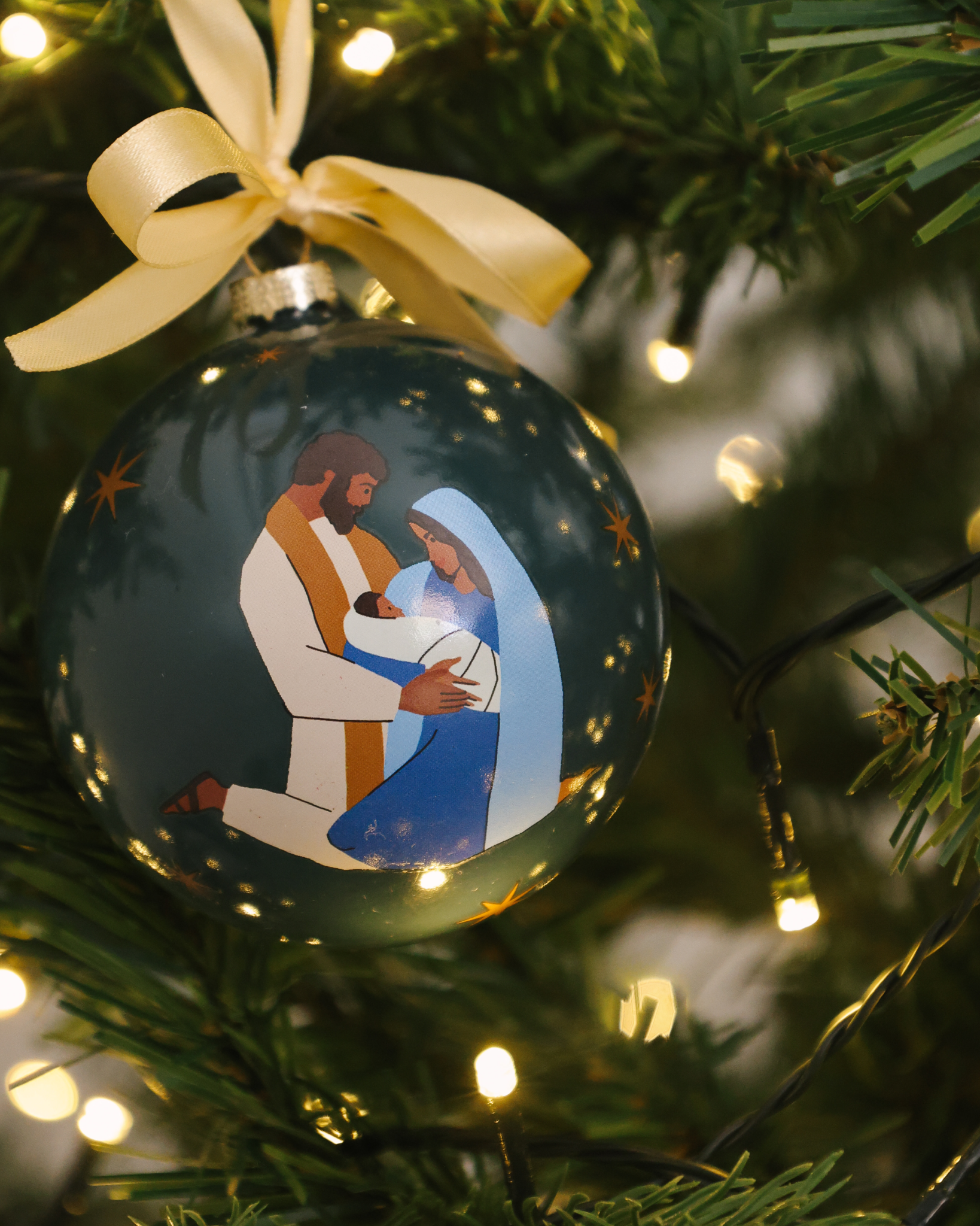 Prince of Peace Christmas ornament with hand-drawn Holy Family—Mary, Joseph, and baby Jesus. Shatterproof plastic with satin ribbon, ideal for families and gifting.