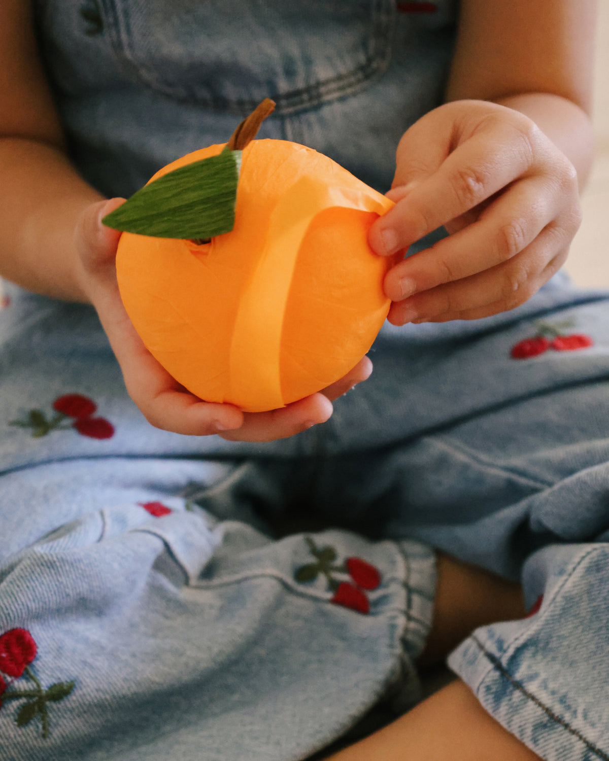 Child holding a St. Nicholas Orange Surprise Ball and pulling the first strip of crepe paper