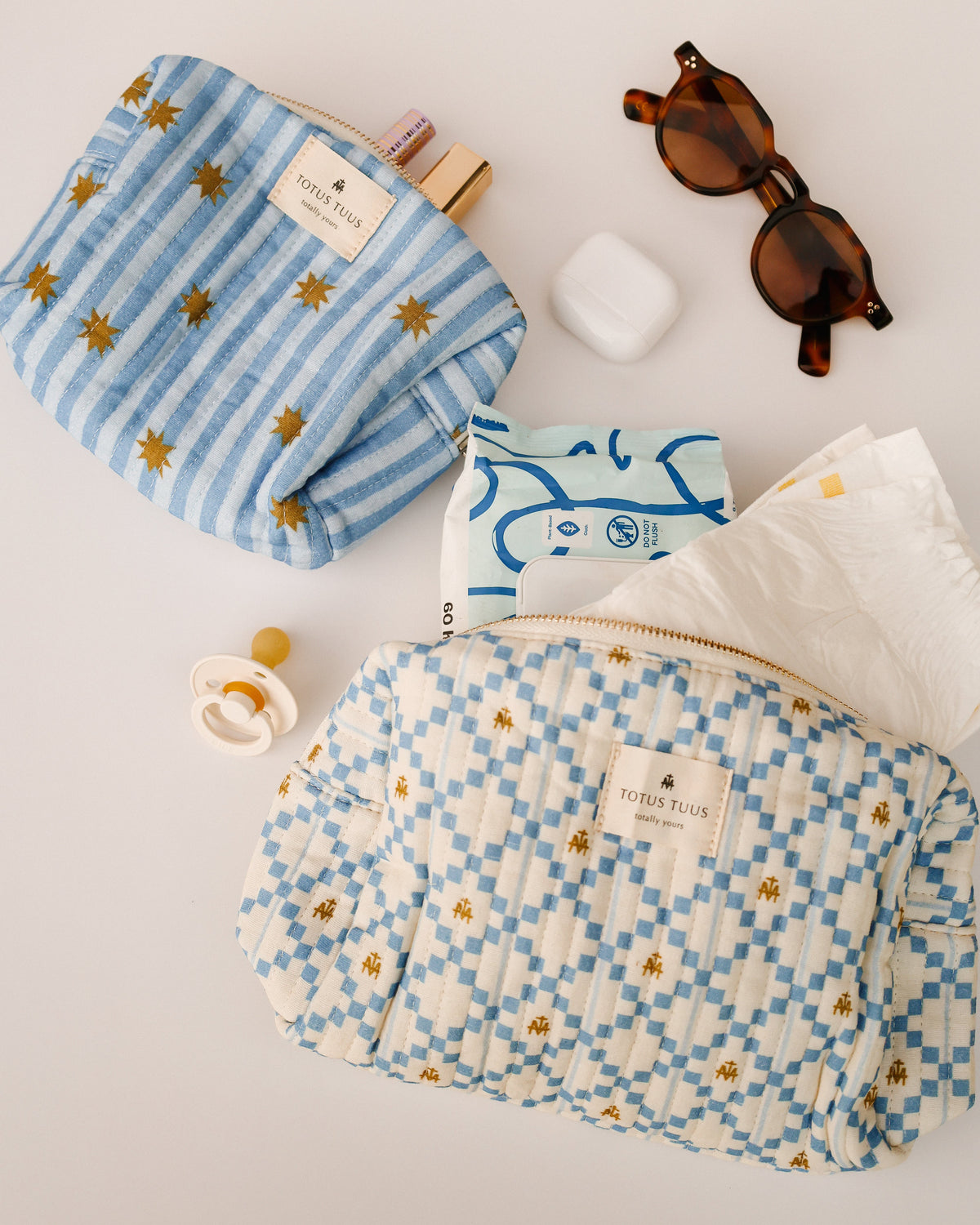 Marian Quilted Toiletry Bag and Marian Stars Striped Make Up Bag with baby wipes, a pacifier and sunglasses