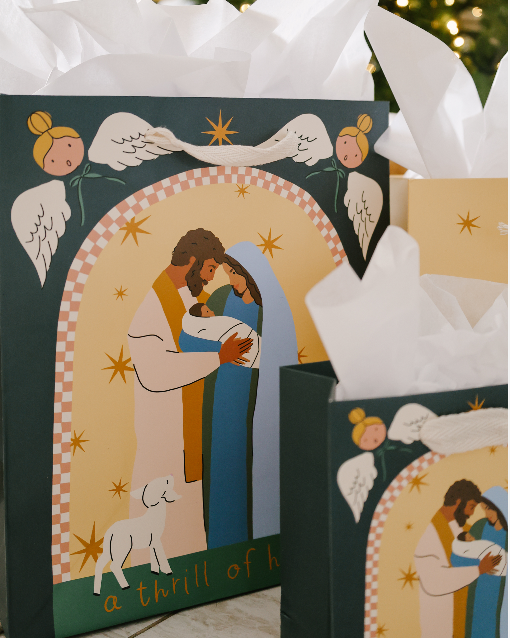 A Thrill of Hope Christmas gift bag set with Nativity illustration of Mary, Joseph, and baby Jesus, angels, and starry sky. Includes 5 bags in 3 sizes with cotton ribbon handles and matching gift tags.