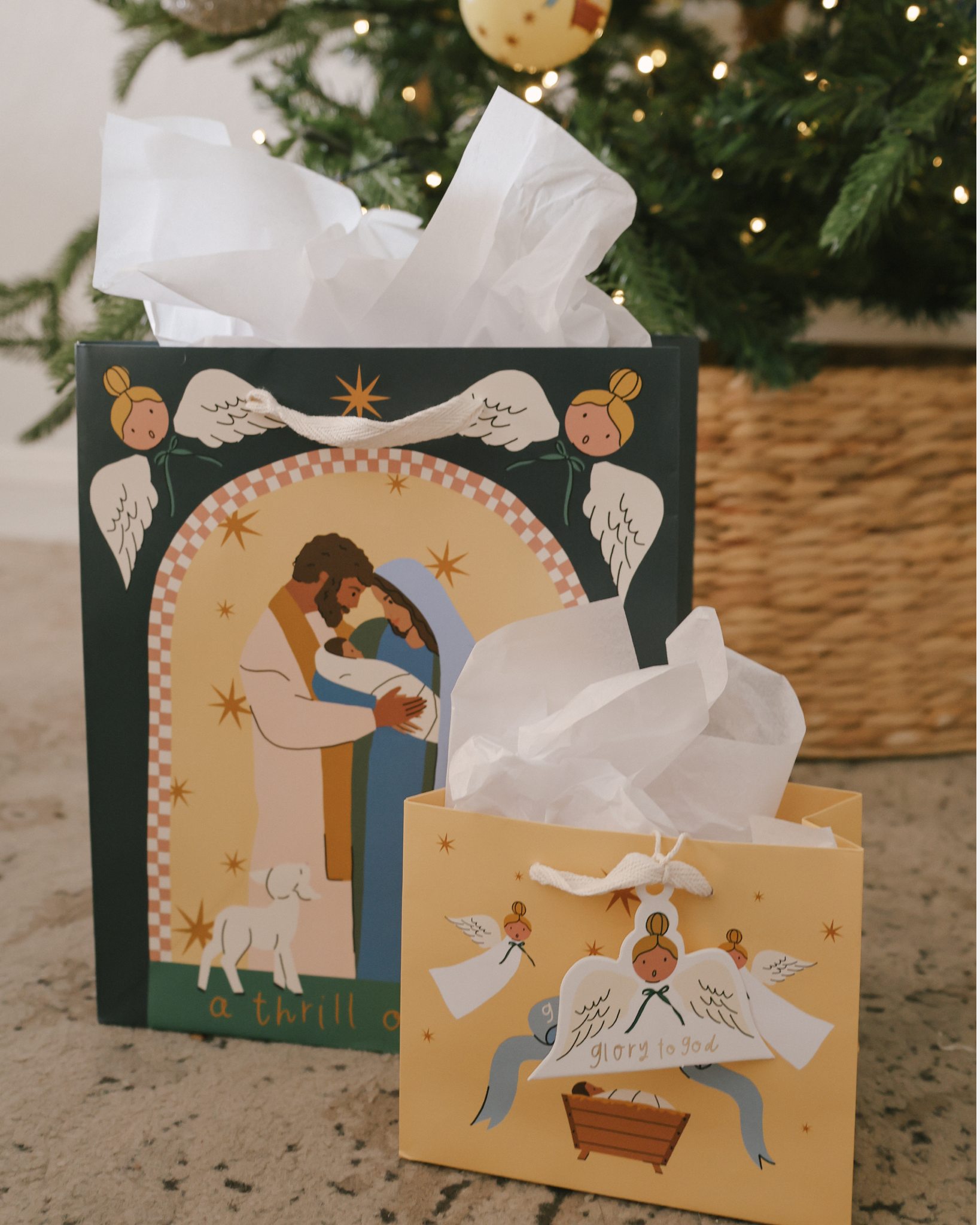Christmas gift bag sets featuring Nativity scenes with baby Jesus, Mary, and Joseph, angels, and starry skies. Includes 5 bags in 3 sizes per set, with cotton ribbon handles and matching gift tags. Designs include 'Glory to God' and 'A Thrill of Hope.'