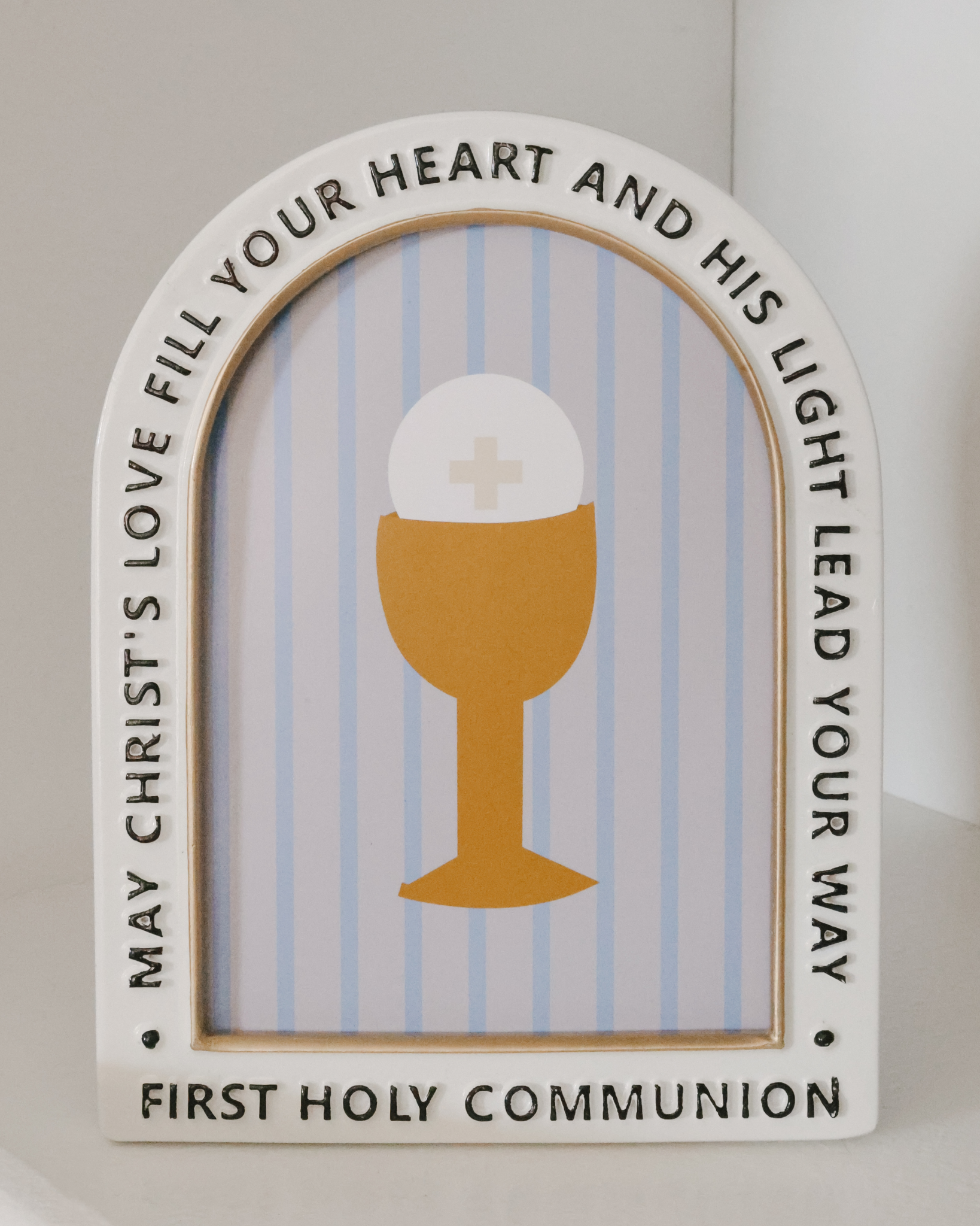 First Communion picture frame with enamel and metal construction, gold chalice and host illustration, soft blue stripes, and blessing inscription. Arched freestanding frame fits 5x7 photo—perfect Christian keepsake gift for children’s First Holy Communion from godparents, grandparents, or parish communities.