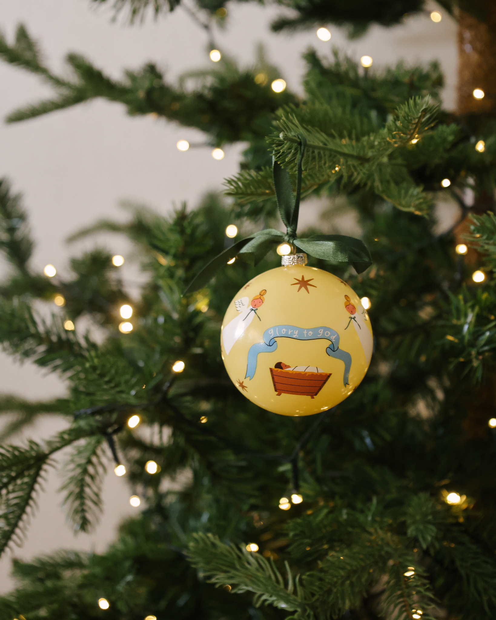 Glory to God Christmas ornament showing baby Jesus in the manger surrounded by angels, with satin ribbon hanger. Made of shatterproof plastic, ideal for families.