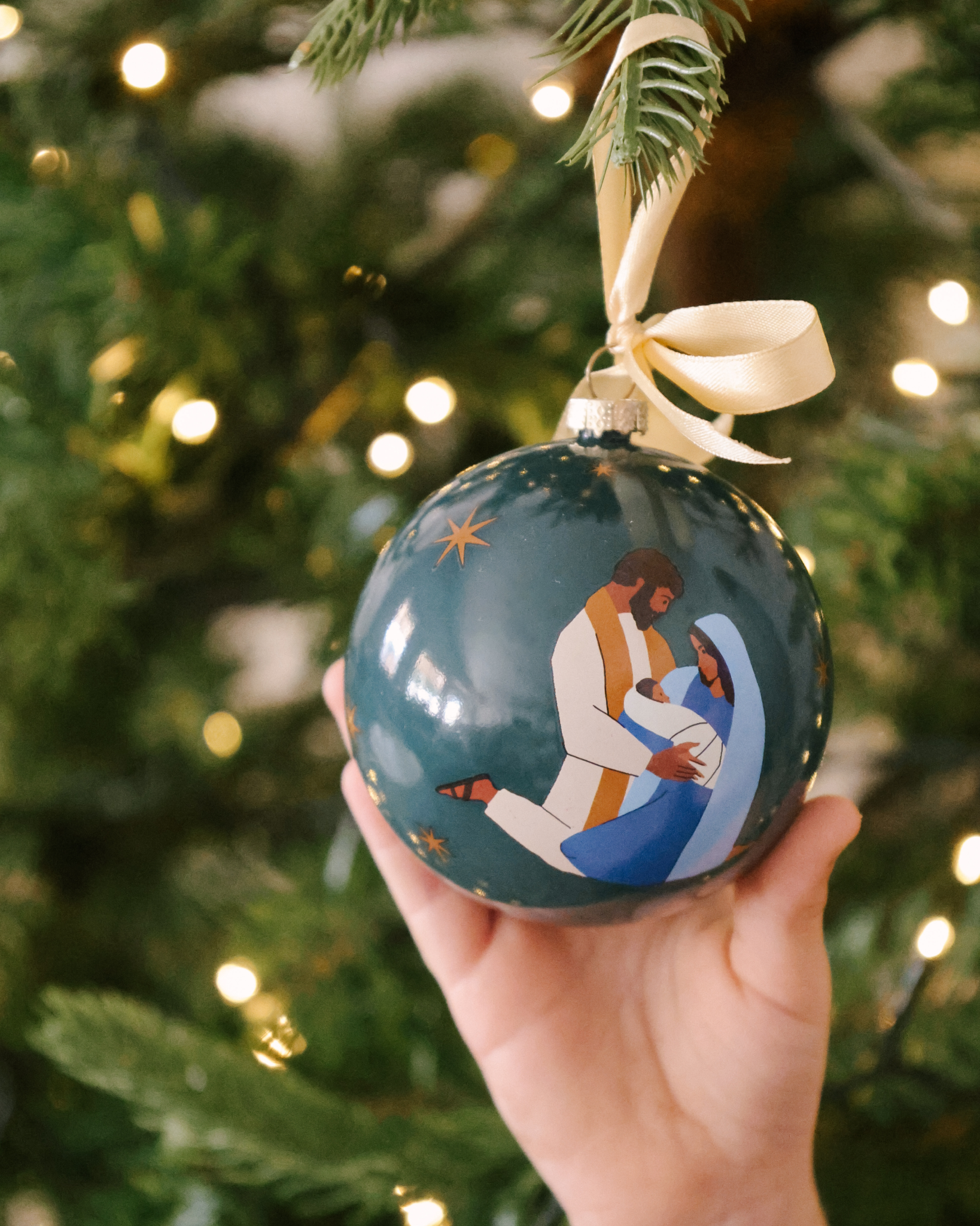 Prince of Peace Christmas ornament with hand-drawn Holy Family—Mary, Joseph, and baby Jesus. Shatterproof plastic with satin ribbon, ideal for families and gifting.