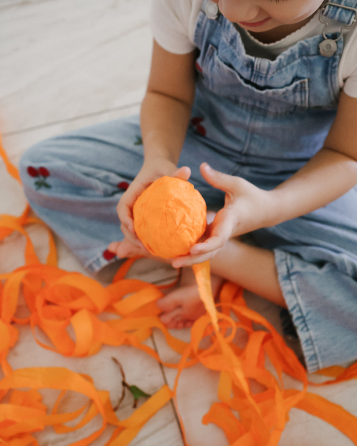 Child unwrapping a St. Nicholas Orange Surprise Ball with orange crepe paper streamers on the floor
