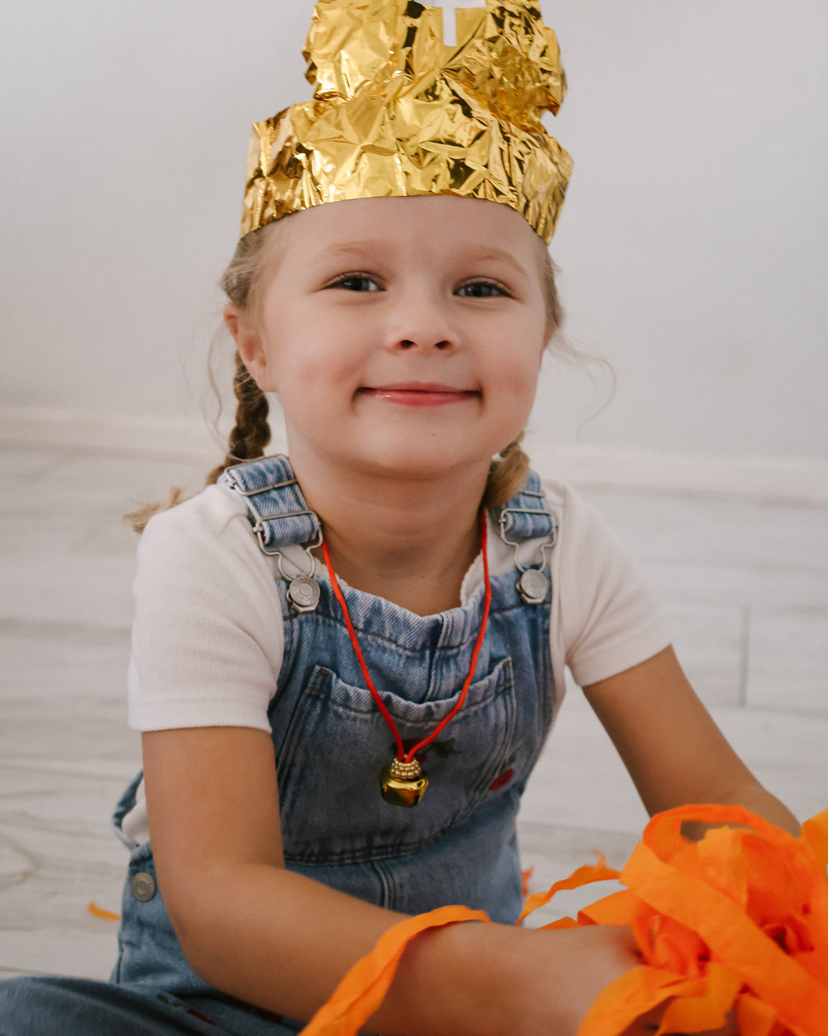 Smiling girl in a gold foil bishop's mitre and jingle bell necklace from her St. Nicholas Orange Surprise Ball