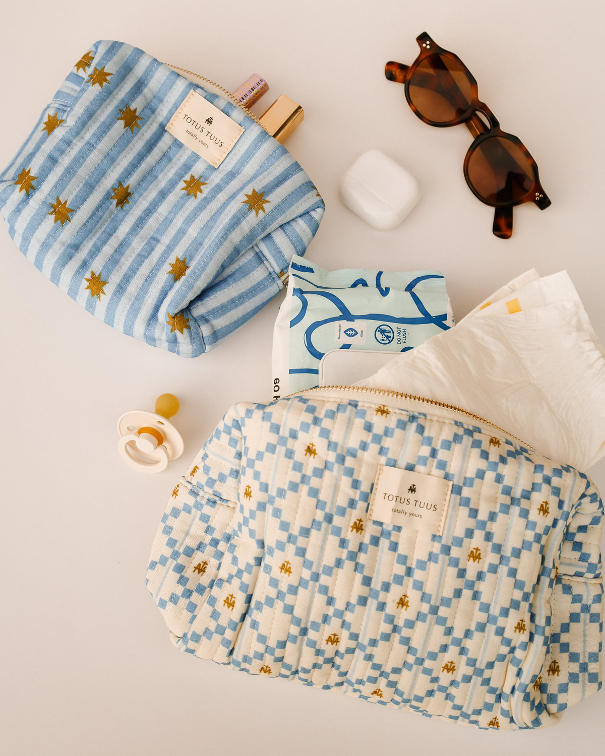 Marian Stars striped make up bag holding lipstick next to the Marian Quilted Toiletry Bag with baby wipes